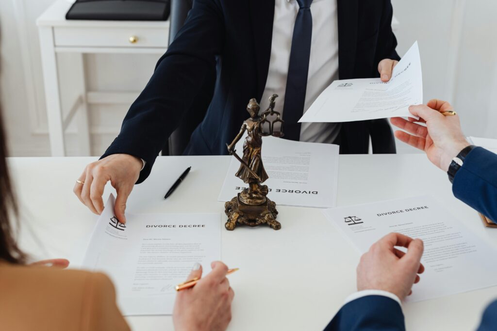 pexels photo 7876051 7876051 Three adults discussing divorce documents in a formal office setting with legal statue in view.